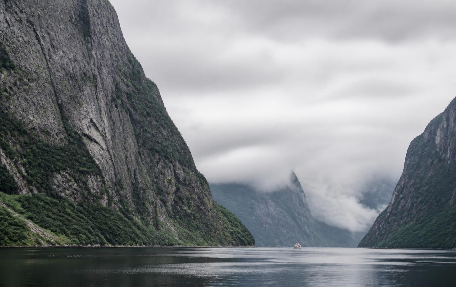 Sheer cliffs rising from the still dark water of Western Brook Pond in Gros Morne National Park, with a small tour boat far below