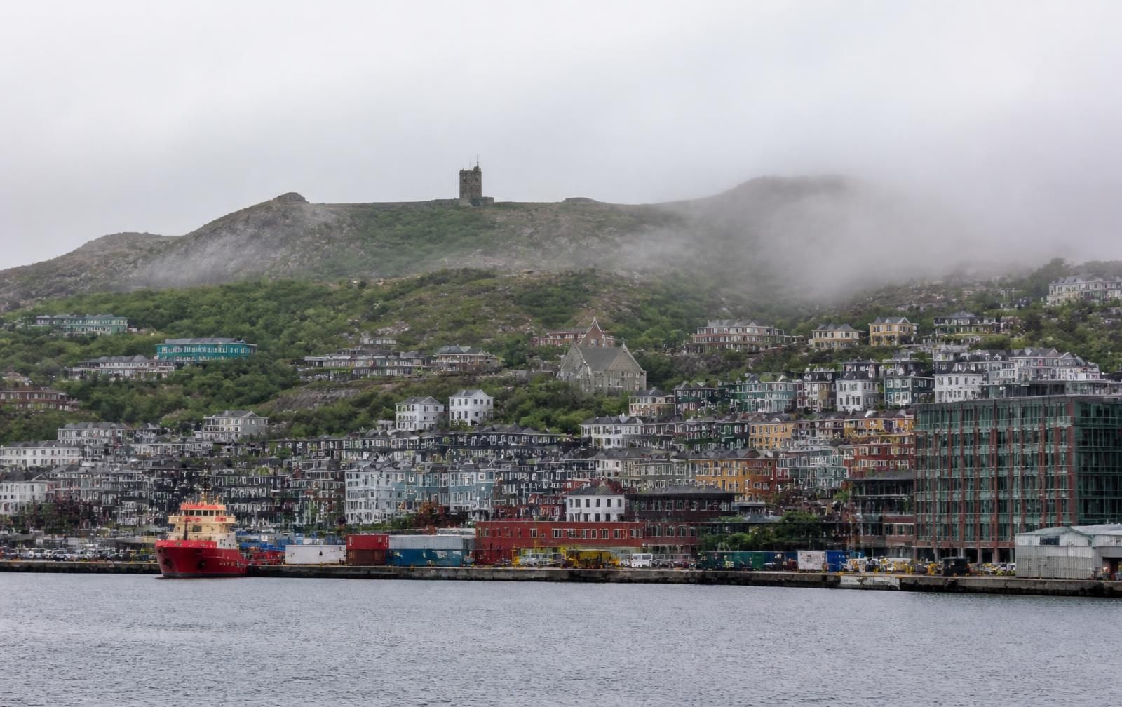 Colourful wooden row houses climbing the hillside above St. John's harbour with Cabot Tower on Signal Hill in drifting fog